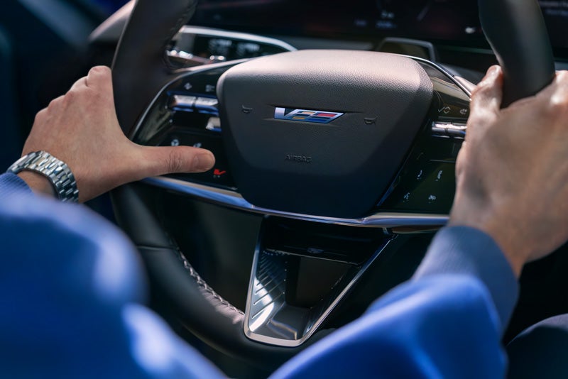 Close-up of a Man About to Press the V-Button on the 2026 OPTIQ-V Steering Wheel | Swickard Cadillac of Thousand Oaks in Thousand Oaks CA